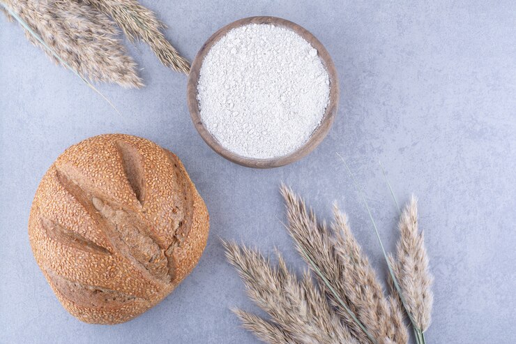 Photo gratuit tiges de plumes séchées, pain de pain et un bol de farine sur la surface en marbre
