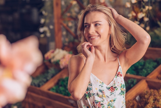 Timide blonde jeune femme avec la main sur sa tête debout dans le jardin