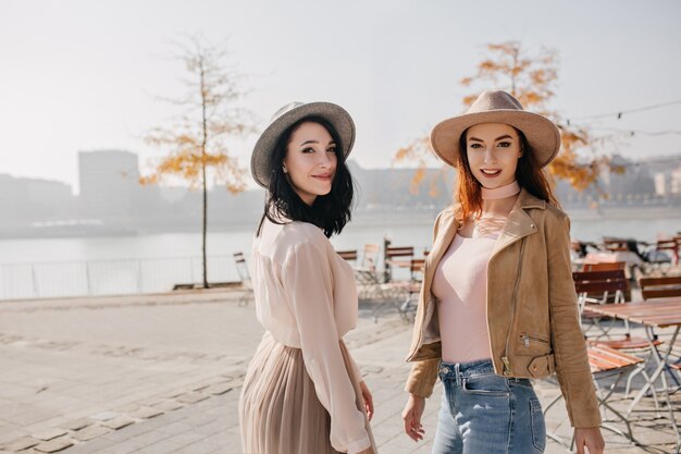 Timide femme brune regardant par-dessus l'épaule en marchant avec un ami