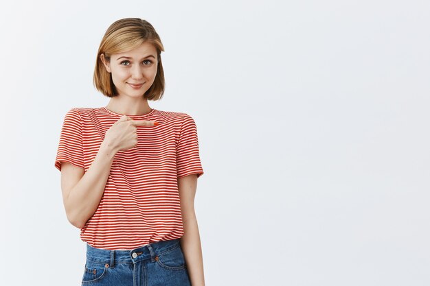 Timide jolie fille pointant le doigt à droite avec une expression modeste