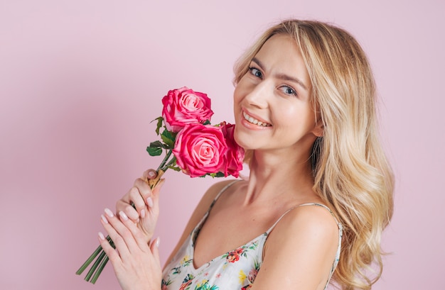 Photo gratuite timide séduisante jeune femme tenant des roses dans la main sur fond rose