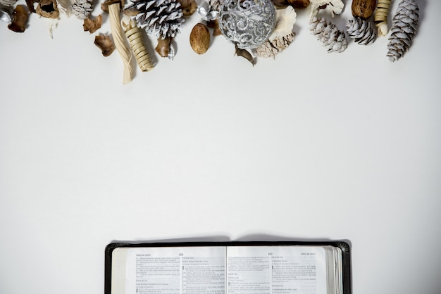 Tir aérien d'une bible ouverte sur une surface blanche avec des pommes de pin et un ornement sur le dessus