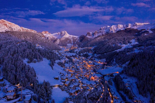 Tir aérien d'une petite ville lumineuse entre les montagnes enneigées pendant la soirée