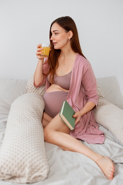 Photo gratuite tir complet femme enceinte pose dans son lit