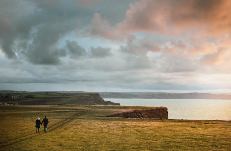 Photo gratuit tir à couper le souffle d'un couple marchant main dans la main sur une falaise au coucher du soleil