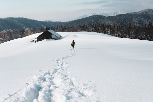 Tir derrière une personne en randonnée dans la montagne enneigée près d'un vieux chalet entouré de sapins