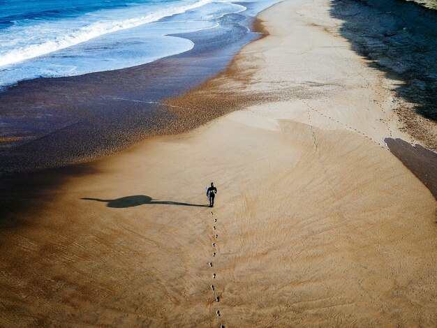 Tir de drone de surfeur marchant sur le rivage