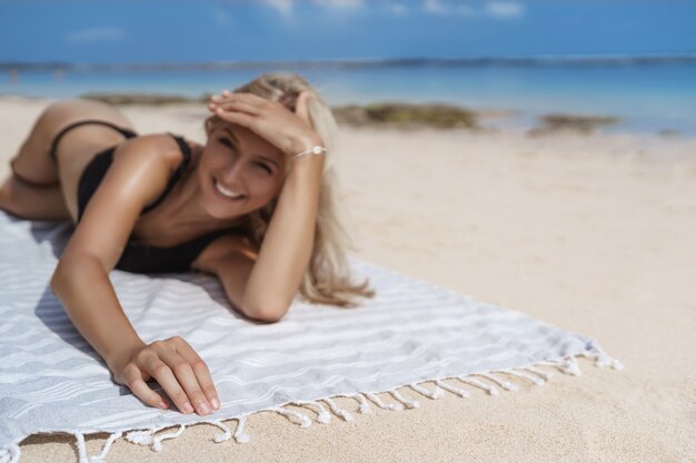 Tir flou charmant bikini noir femme blonde souriant joyeusement.