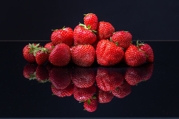 Tir horizontal d'un tas de fraises croates rouges sur une surface réfléchissante noire