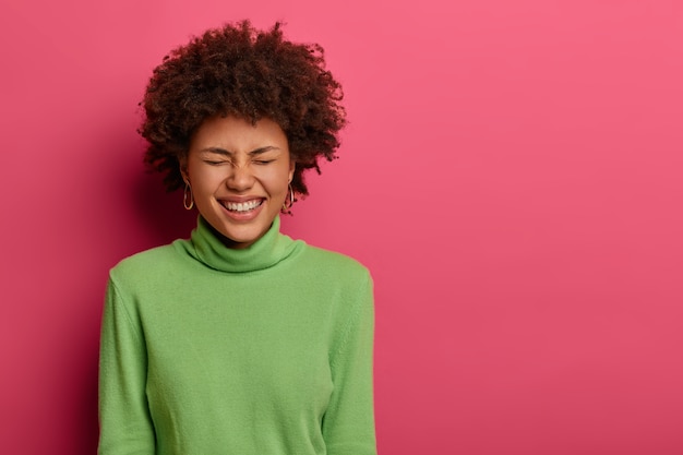 Tir à l'intérieur d'une femme afro-américaine surémotivée se moque d'une blague, ferme les yeux de joie, a ravi l'expression du visage