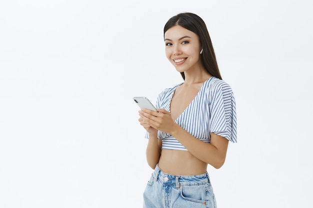 Tir à l'intérieur d'une femme asiatique heureuse attrayante sociable en haut recadrée holding smartphone