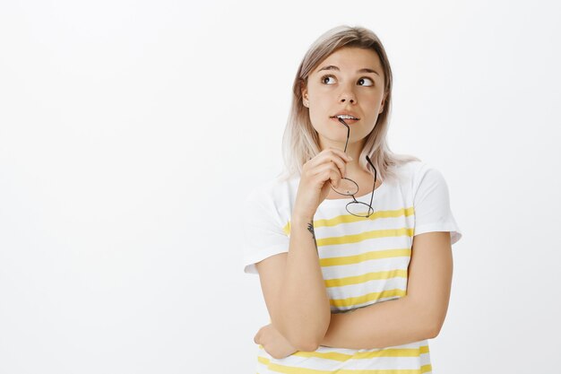 Tir intérieur d'une fille blonde rêveuse avec des lunettes posant dans le studio