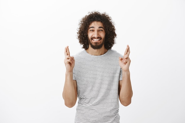 Tir à l'intérieur d'un homme barbu oriental croyant anxieux avec une coiffure afro, levant les doigts croisés et grimaçant de nervosité, voulant réaliser un souhait