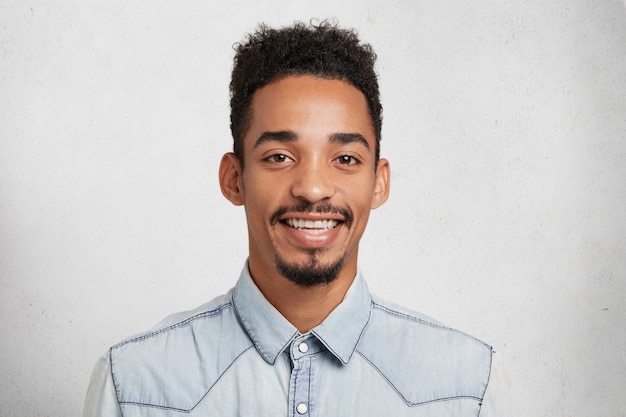 Tir intérieur d'un jeune homme barbu heureux et moustache, porte une chemise en jean, sourit joyeusement