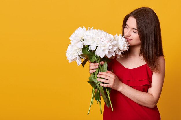 Tir intérieur de jolie tendre douce dame en robe rouge posant isolé sur jaune