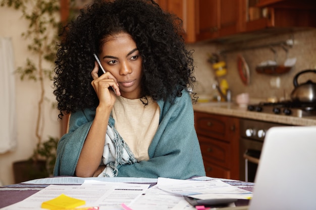 Photo gratuite tir intérieur de la malheureuse jeune femme aux cheveux bouclés ayant une conversation téléphonique sérieuse