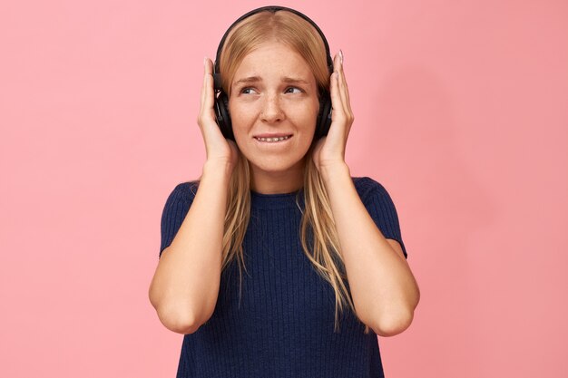 Tir isolé d'une adolescente mignonne tenant la main sur les oreilles, bénéficiant de morceaux de musique de haute qualité dans un lecteur mp3 à l'aide d'un casque sans fil