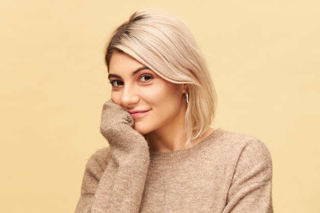 Tir isolé d'une adorable jeune femme européenne avec une coiffure bob teinte avec un sourire joyeux curieux, tenant la main sous le menton, écoutant attentivement. Concept de personnes et de style de vie