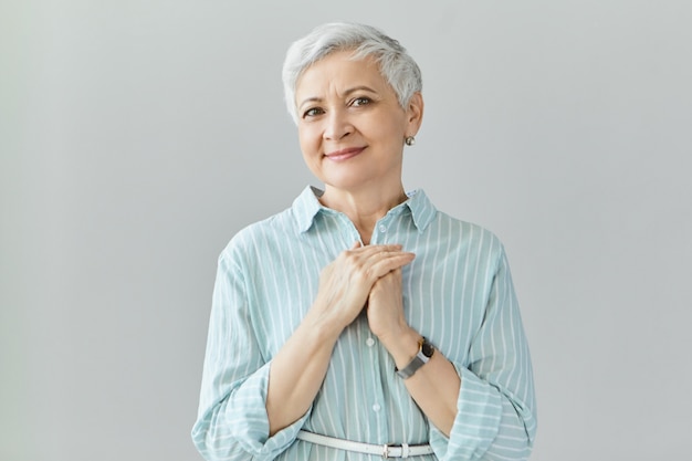 Tir isolé de la belle dame européenne mature émotionnelle avec une coiffure de lutin tenant les mains sur sa poitrine, remplie d'émotions heureuses. Aime la gentillesse, la gratitude, la reconnaissance et le concept d'appréciation