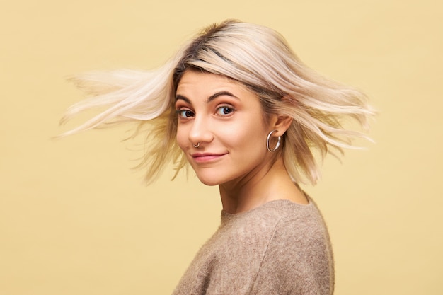 Tir isolé de la belle jeune femme incroyable en pull surdimensionné élégant se retournant avec des cheveux blonds qui coule dans le vent