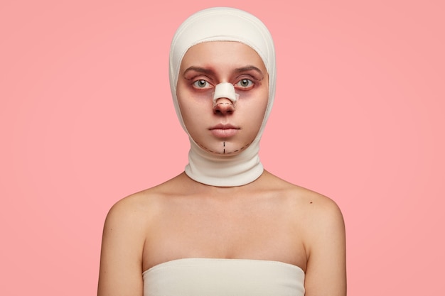 Tir isolé d'une fille a les épaules nues, le visage marqué en lignes, enveloppé d'un bandage, préparé pour le traitement du visage