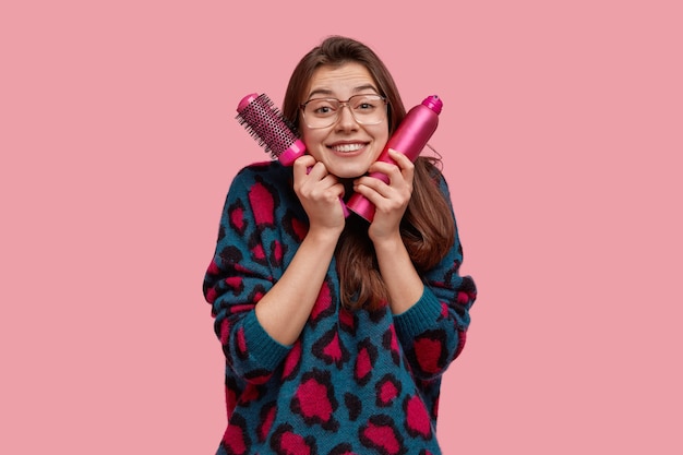 Tir isolé de l'heureuse jeune femme aux cheveux noirs, conserve les choses nécessaires pour faire la coiffure près du visage