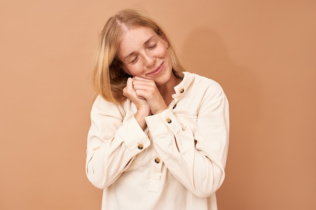 Tir isolé de la jolie jeune femme européenne heureuse, plaçant le visage sur les mains, faisant la sieste, souriant doucement, voyant de bons rêves agréables la nuit