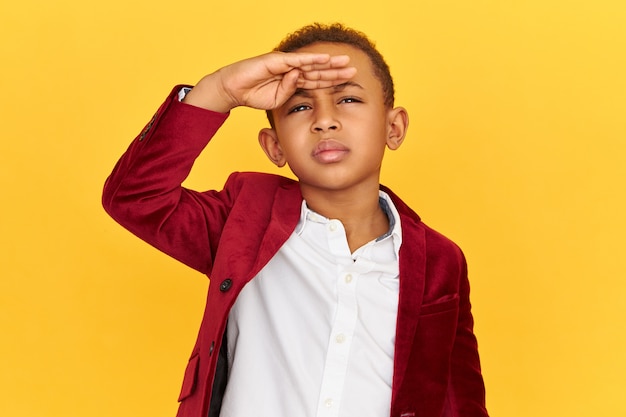 Photo gratuite tir isolé d'un petit garçon afro-américain ayant concentré une expression faciale concentrée regardant vers le haut avec la main sur le front et fronçant les sourcils, essayant de voir quelque chose plus clairement