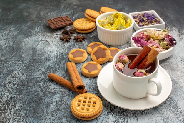 Tir latéral d'une tasse de tisane avec des fleurs sèches et des biscuits et des cannelles sur fond gris