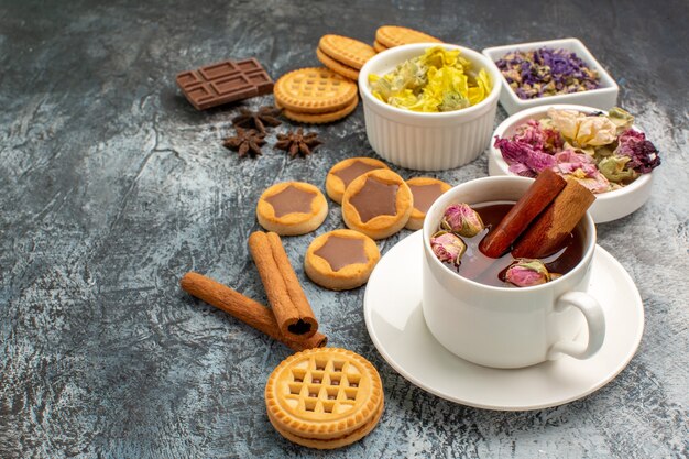 Tir latéral d'une tasse de tisane avec des fleurs sèches et des biscuits et des cannelles sur fond gris