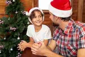 Photo gratuite tir moyen garçon avec père assis près de sapin de noël