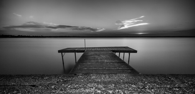 Tir en niveaux de gris d'un chemin en bois sur la mer sous un ciel clair