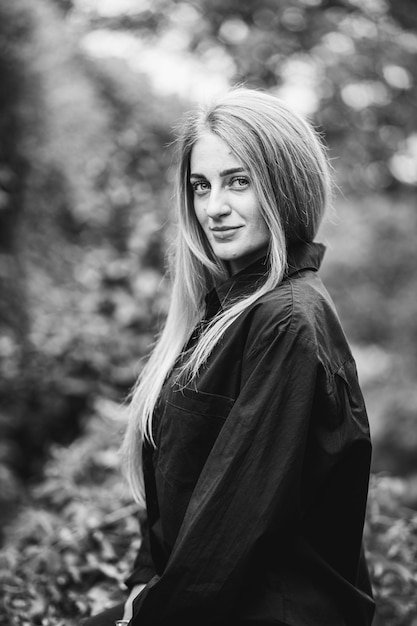 Tir en niveaux de gris d'une femme blonde caucasienne à la mode posant entourée de verdure