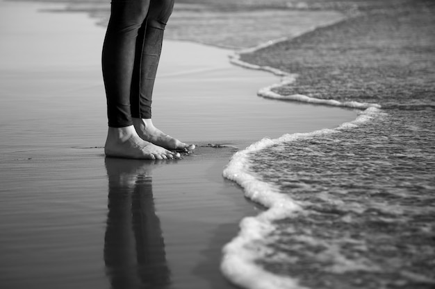 Tir en niveaux de gris des jambes pieds nus de l'homme debout sur une plage de sable