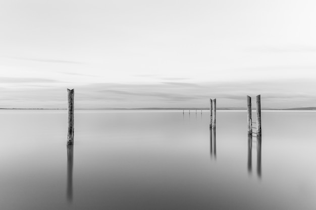 Tir en niveaux de gris d'une jetée en bois près de la mer sous le beau ciel nuageux