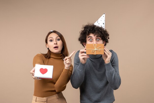 Tir de nouvel an avec jeune couple porter chapeau de nouvel an fille avec coeur et cadeau de pointage dans la main de gars sur fond gris