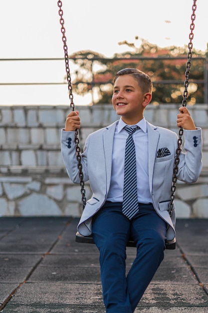 Tir vertical d'un adorable enfant mâle dans une tenue de costume formel posant sur une balançoire