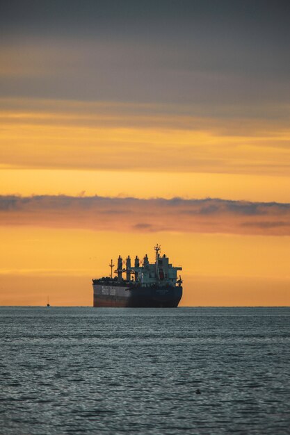 Tir vertical de l'ancien navire dans un lac sous le ciel coloré pendant le coucher du soleil