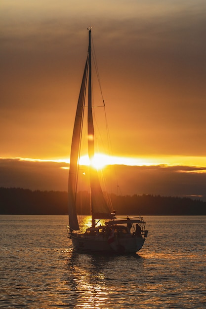 Tir vertical d'un bateau à voile dans l'océan pendant le coucher du soleil