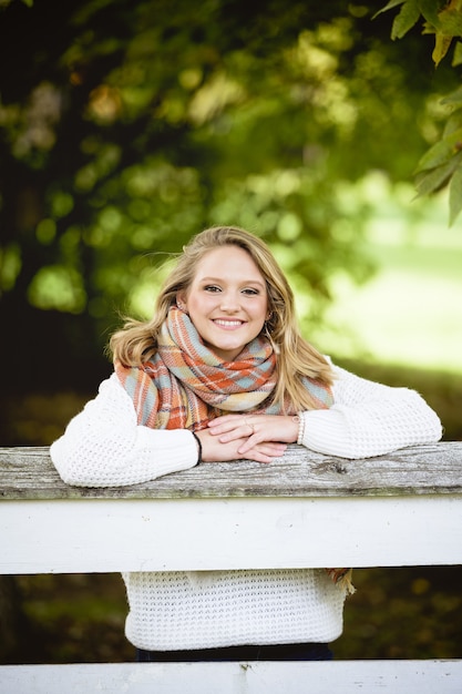 Tir vertical d'une belle femme blonde souriante s'appuyant sur une bordure en bois