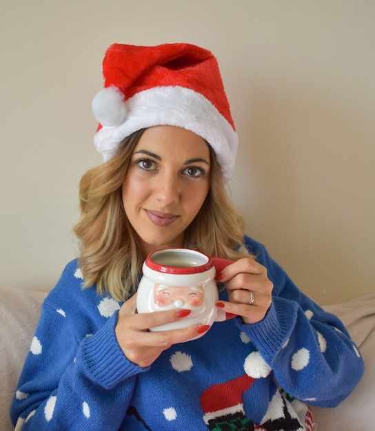 Tir vertical d'une belle jeune femme portant une robe de Noël et un chapeau tenant une tasse de Santa