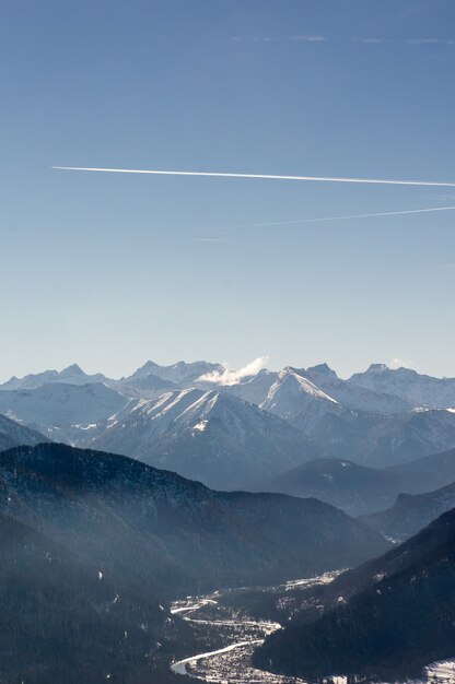 Tir vertical de belles chaînes de montagnes sous un ciel lumineux avec des traînées de moteur