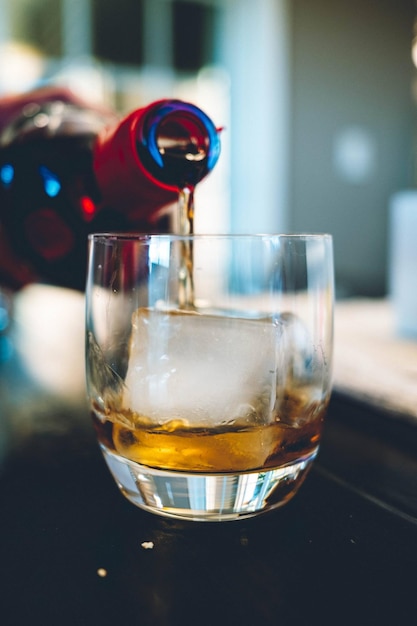 Photo gratuite tir vertical d'une bouteille de boisson alcoolisée versante dans un verre avec une glace