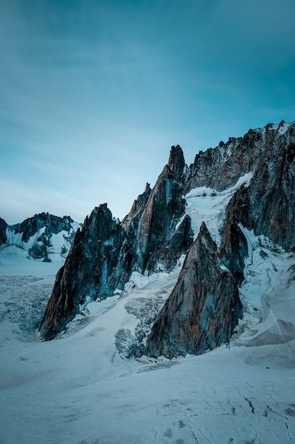 Tir vertical d'une colline enneigée près de la montagne sous un ciel bleu