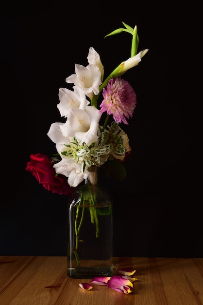 Tir vertical de différentes fleurs dans un pot sur une surface en bois avec un fond noir