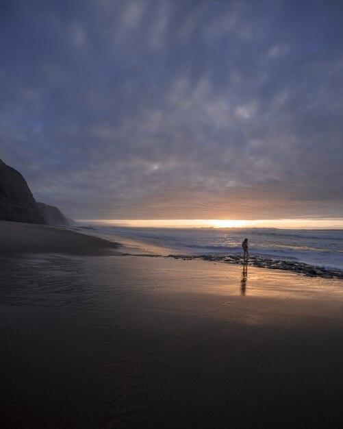 Tir vertical du bord de mer sur un beau coucher de soleil avec un jeune garçon marchant sur la mer