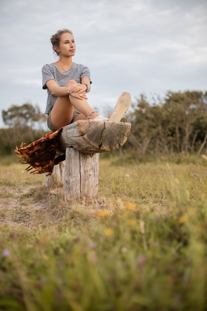 Photo gratuite tir vertical d'une femme assise sur un morceau de bois dans le domaine