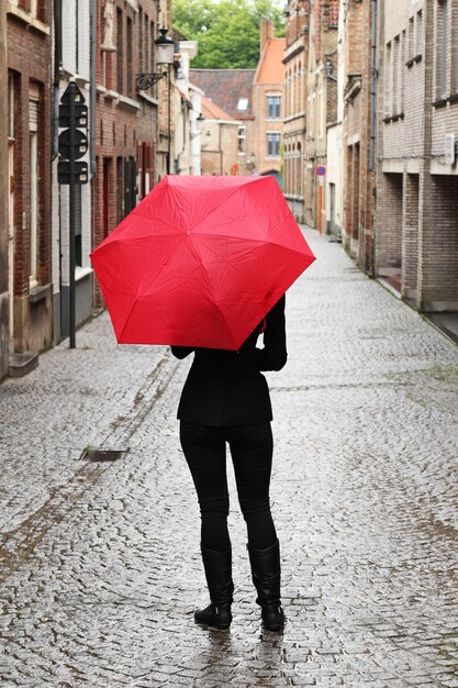 Tir vertical d'une femme avec un parapluie rouge dans la rue