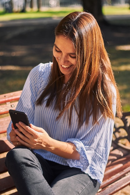 Tir vertical d'une fille assise sur le banc et regardant son téléphone