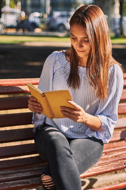 Tir vertical d'une fille dans une chemise bleue lisant un livre sur le banc